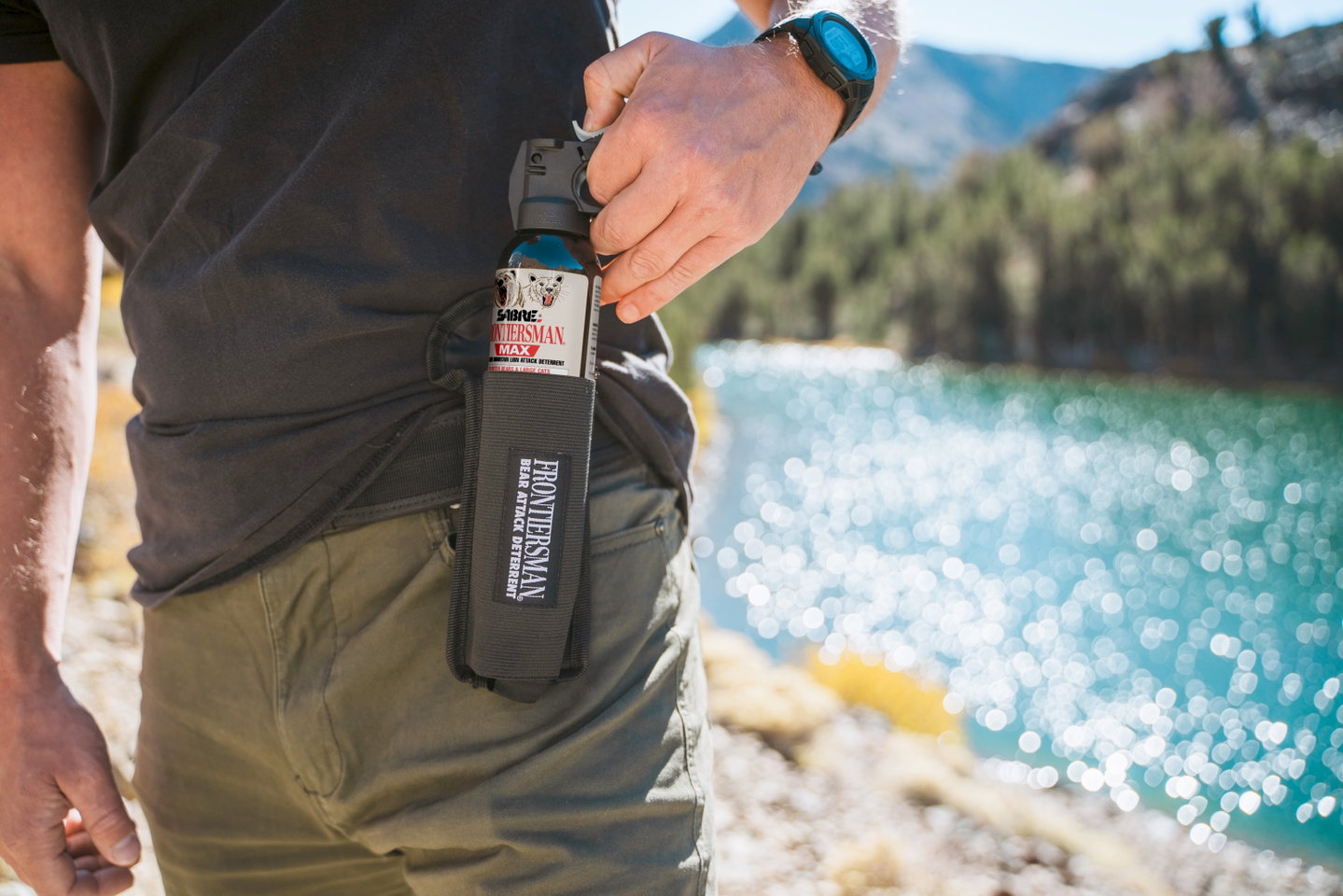 Hiker with SABRE bear spray in a belt holster on a lakeside trail