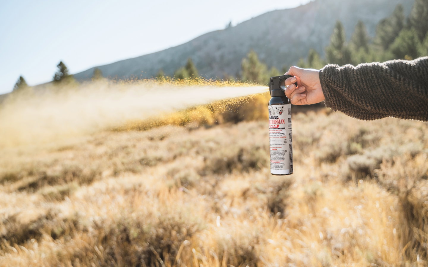 SABRE bear spray being sprayed across a grassy mountain meadow