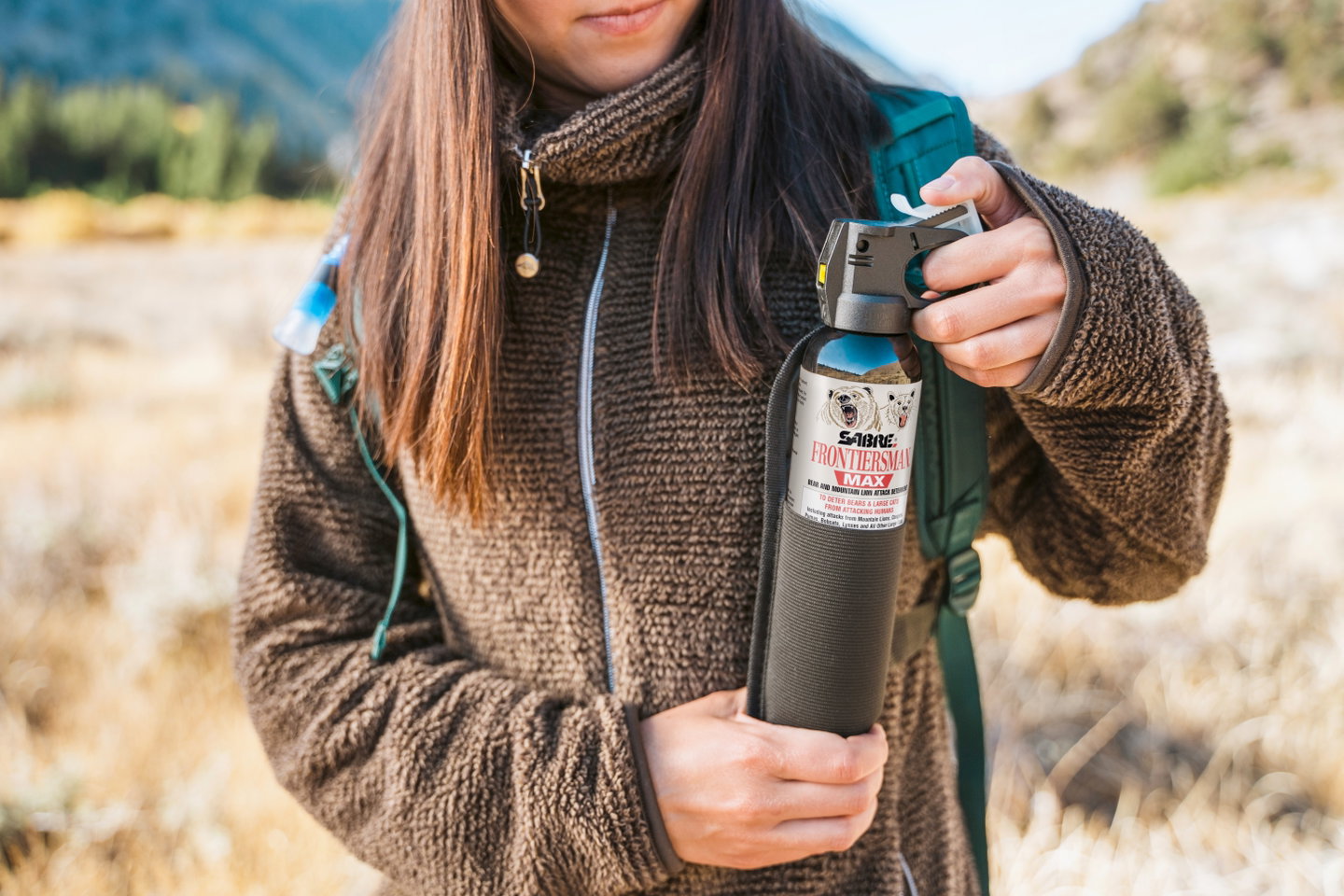 Hiker in a fleece jacket holding SABRE FRONTIERSMAN MAX bear spray on a fall trail