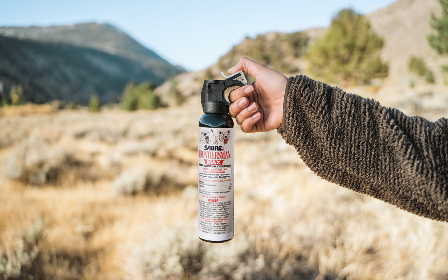 Hand holding a can of SABRE FRONTIERSMAN MAX bear spray in open country