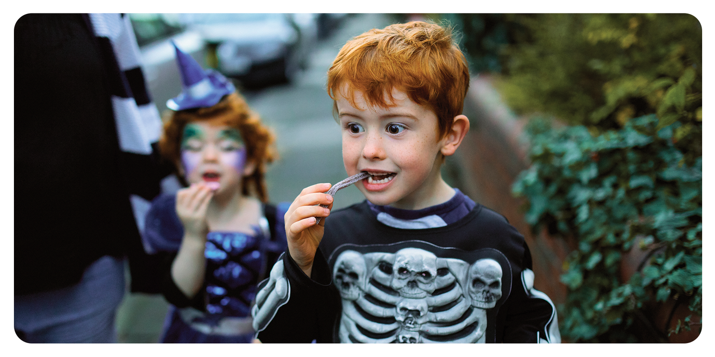 Boy in a skeleton costume eating candy while trick or treating