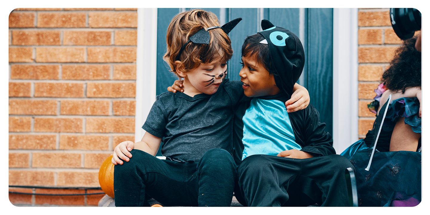 Two young boys in cat costumes with face paint sitting together on a front step